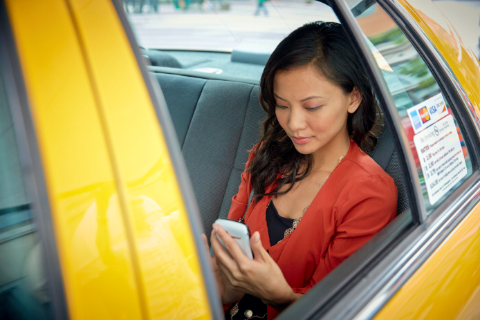 Two colleagues actively engaged in conversation view information on their tabletsA young woman sitting in the back of a yellow cab checks her mobile phone