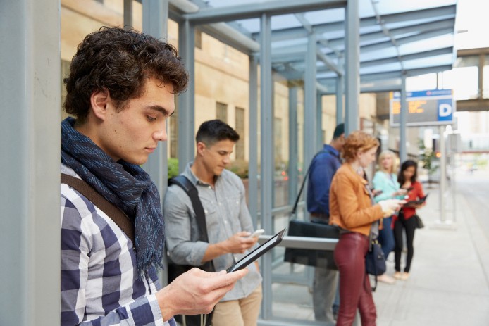 A young man standing with others at a bus stop tracks his shipment on his mobile phone