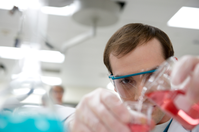 Man pours reddish liquid into container in lab