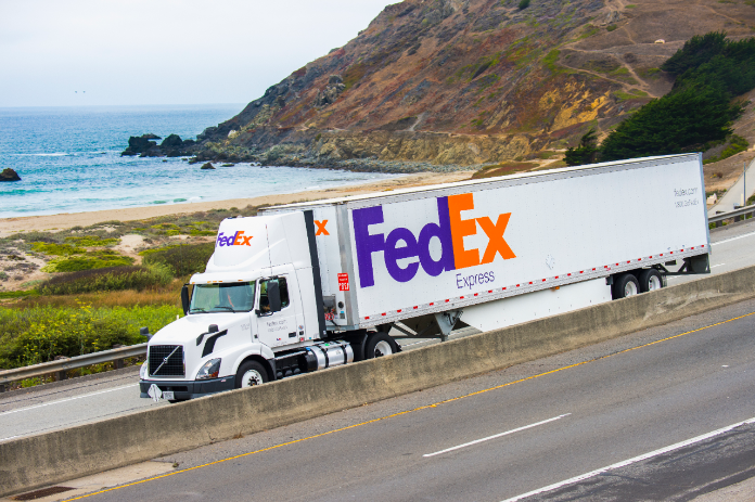 A FedEx semi truck drives along a coastal highway.