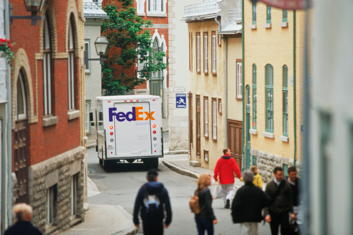 A FedEx Ground truck drives down an apartment-lined street.