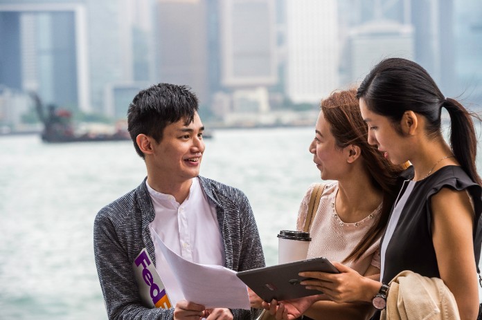 A young man holding a FedEx envelope stops to offer directions to two women