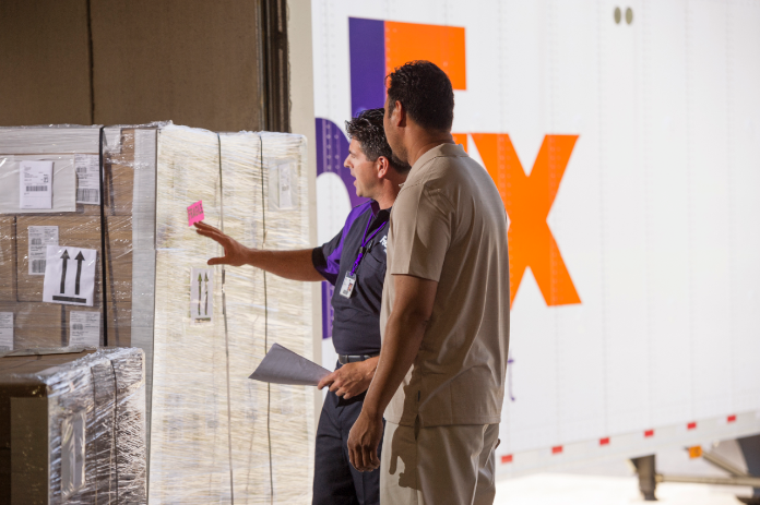 A FedEx courier chats with a customer and points to the freight shipment he just dropped off.