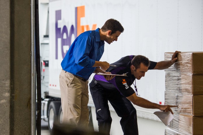 FedEx Freight driver and shipping dock employee looking at palletized, stacked freight