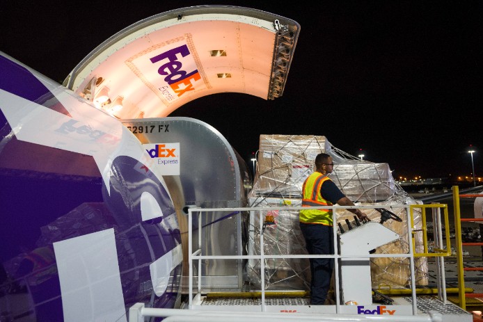 A FedEx Express courier loads a pallet onto a FedEx Express plane.