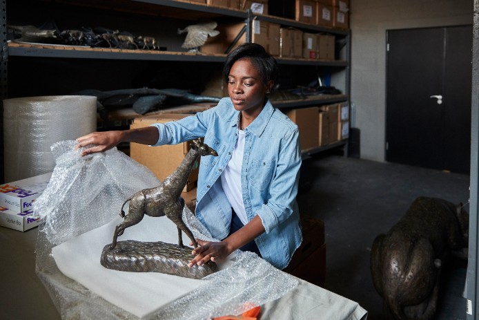 A woman unwraps an expensive tabletop sculpture of a giraffe.