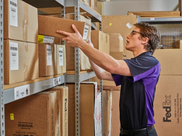 A FedEx courier places a package on a warehouse shelf.