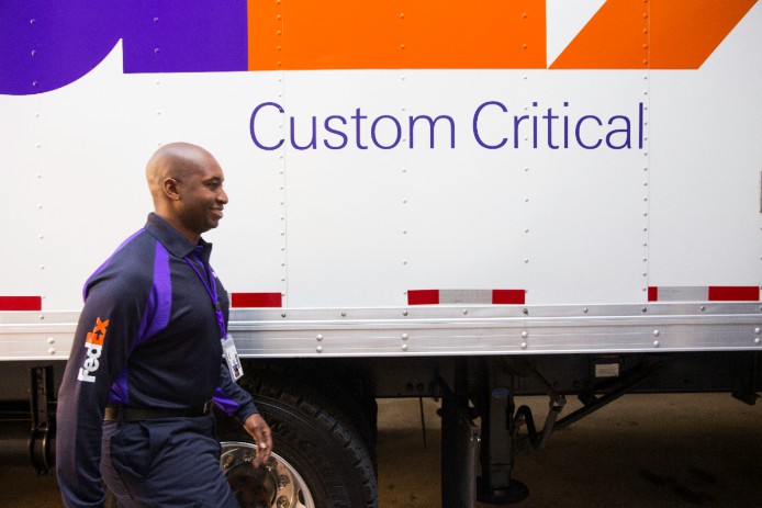 Courier walks beside FedEx Custom Critical truck