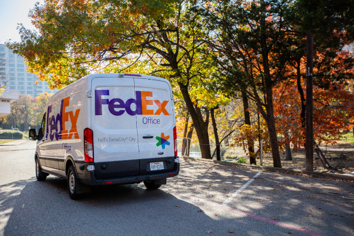 FedEx Office van drives on street lined with trees in fall colors
