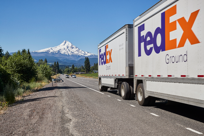 FedEx Ground truck drives with snow-covered mountain in background