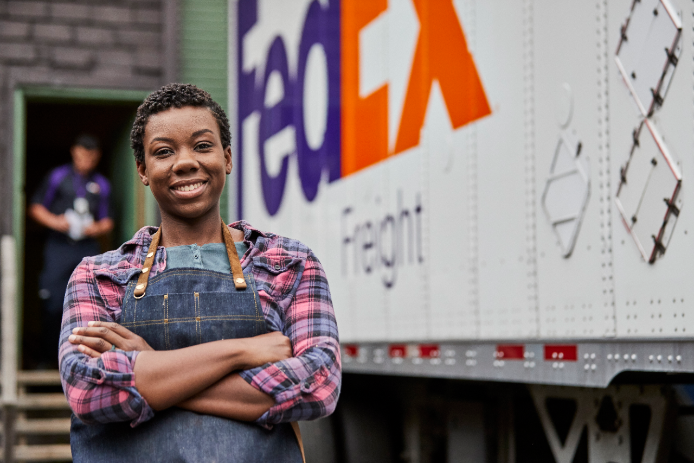 female small business owner standing and smiling confidently next to a FedEx Freight trailer