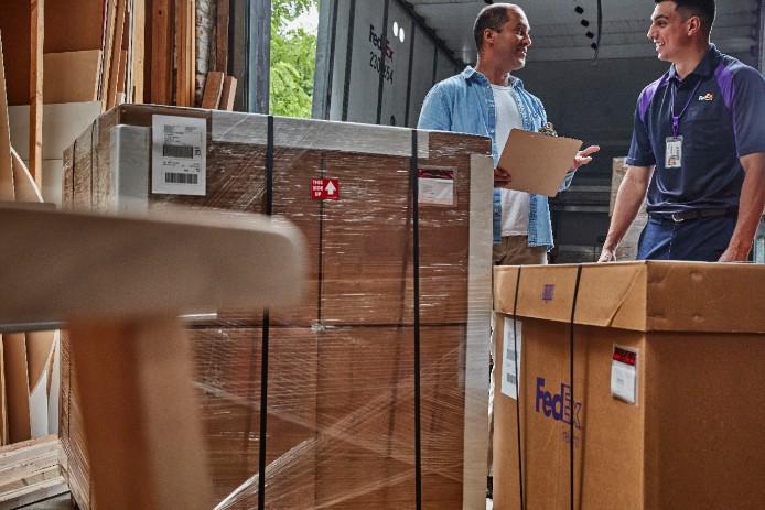 A business owner holds his customs documents and chats with a FedEx courier on a loading dock.