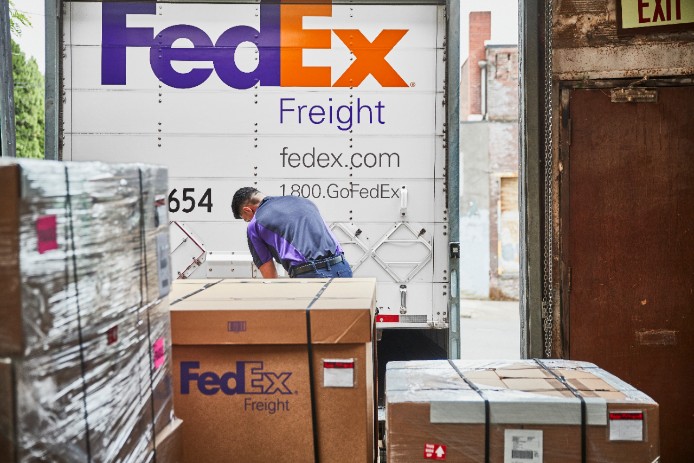 A courier standing at a loading dock locks the rear door of a FedEx Freight trailer