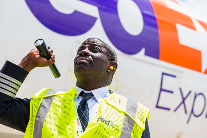 A customs agent stands next to a FedEx Express delivery van.