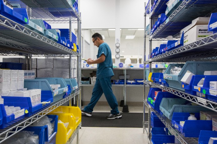 Man walks between shelves lined with pharmaceuticals
