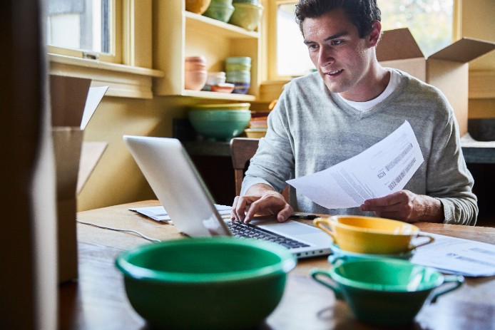 A retailer who sells ceramic bowls sits at his laptop and types in details from a shipping label.