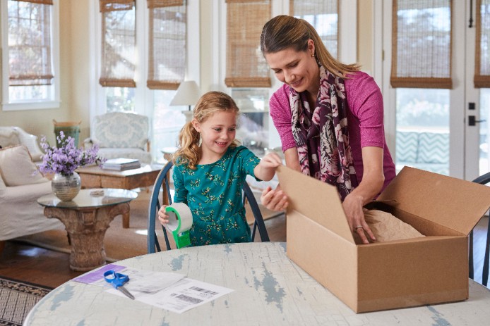 Woman and daughter at home packing shipment in box