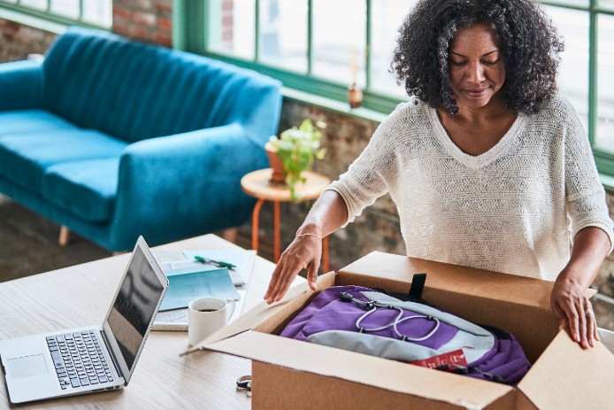 A woman peers inside a newly-opened package filled with purple and gray backpacks