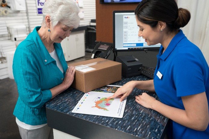 Pack-and-ship store owner looking over a FedEx delivery transit map with a customer.