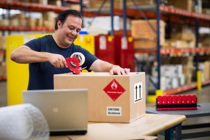 man taping a box with a dangerous goods symbol man taping a box with a dangerous goods symbol