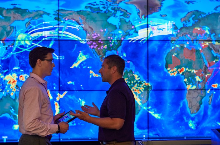 men talking in front of large digital weather map