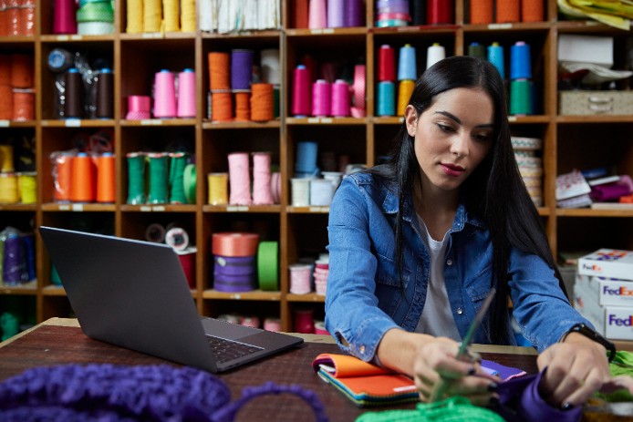 Woman looking at a spool of yarn with a laptop beside her