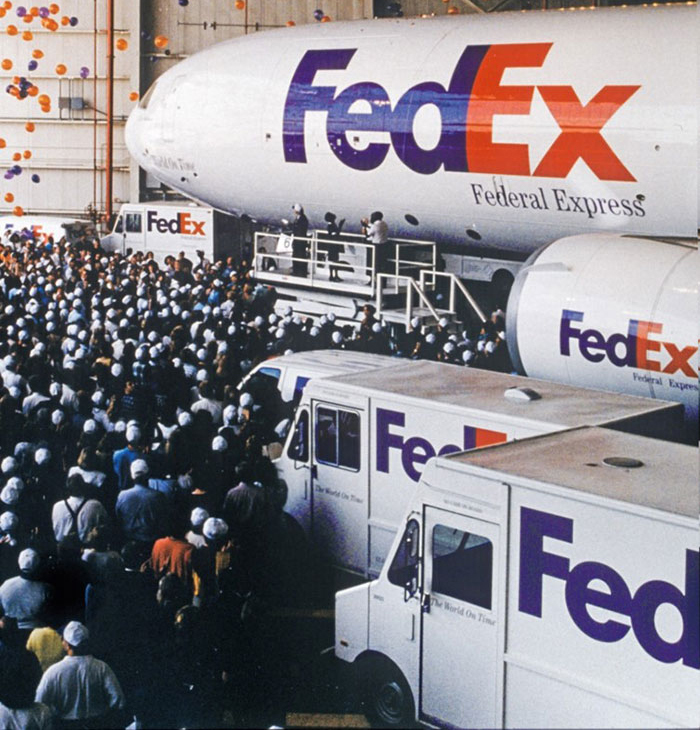 Grupo de empleados de FedEx celebrando en un hangar con un camión y un avión