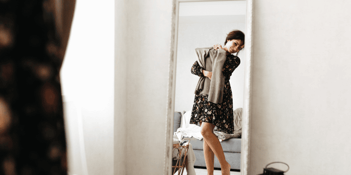 A woman stands in front of a mirror, checking how a piece of clothing looks on her. 