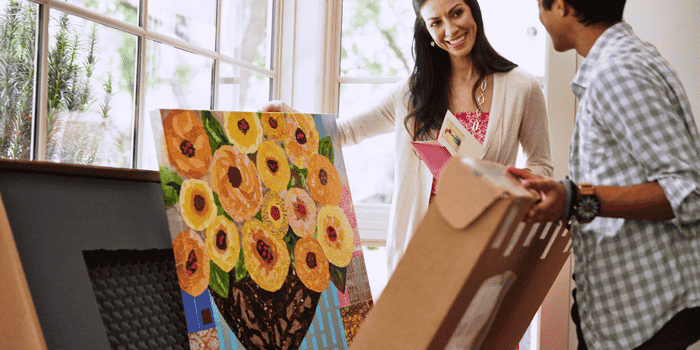 A woman unpacks a delivered painting from a shipping box. 