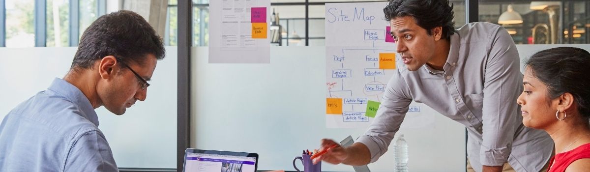 Trois collègues travaillent ensemble autour d’une table, entourés de notes, d’un ordinateur portable et d’un tableau blanc