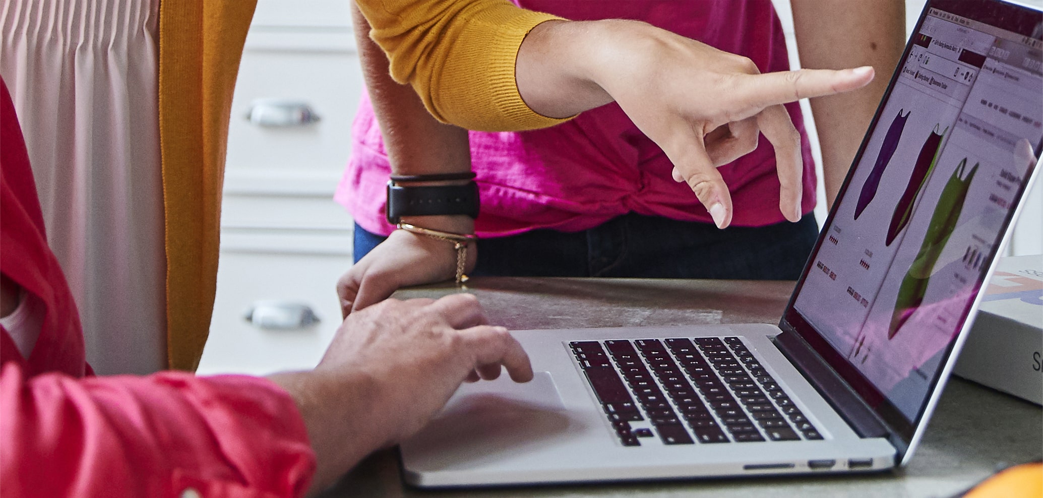 Grupa kobiet zgromadzona wokół komputera, przeglądająca i wybierająca kostiumy kąpielowe w Internecie. 