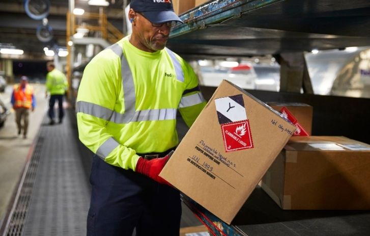 Homme portant un colis sur lequel une étiquette indique qu’il contient du liquide inflammable