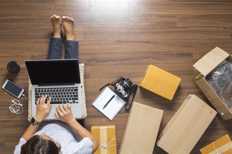 Person using a laptop on the floor surrounded by boxes and tech gear