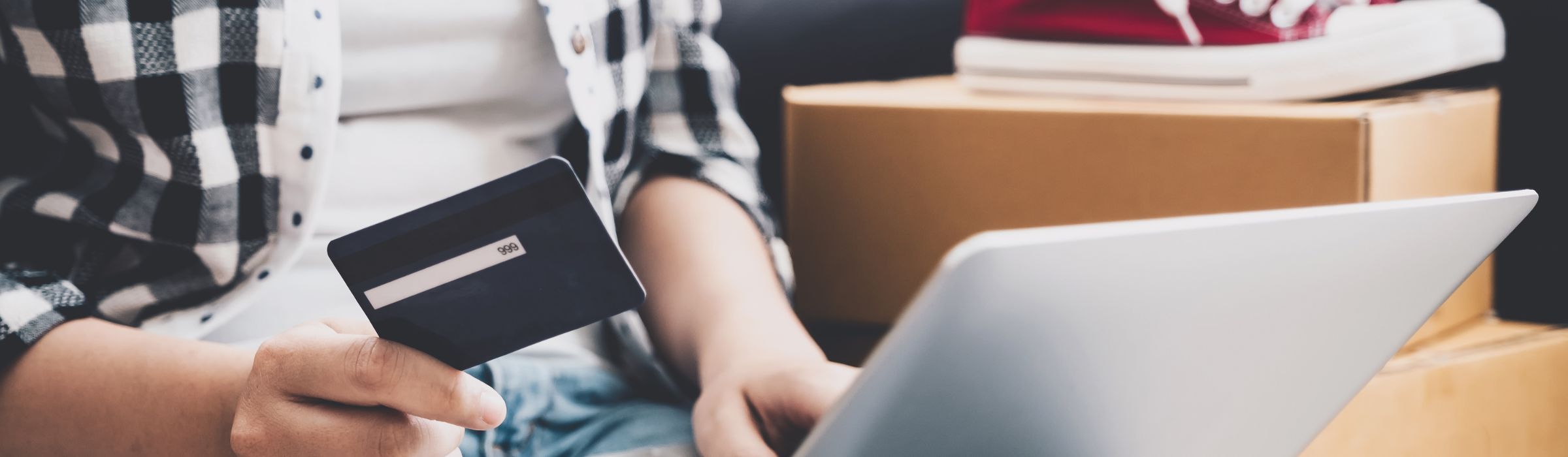 Un homme assis sur un canapé, utilisant un ordinateur portable, une carte bancaire à la main.