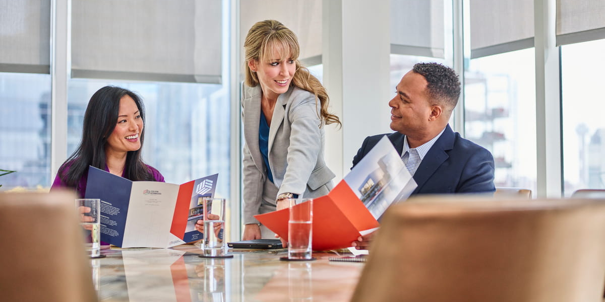 Three colleagues around a conference table reviewing a couple of folders in a bright modern office. 
