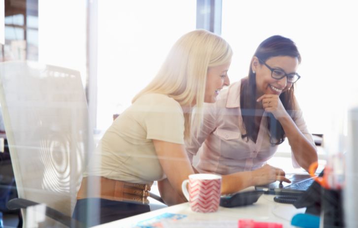 Two women sitting together, smiling, looking at a laptop.