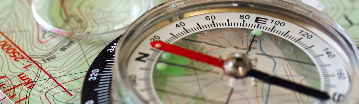 Compass with red and black needles resting on a topographic map.