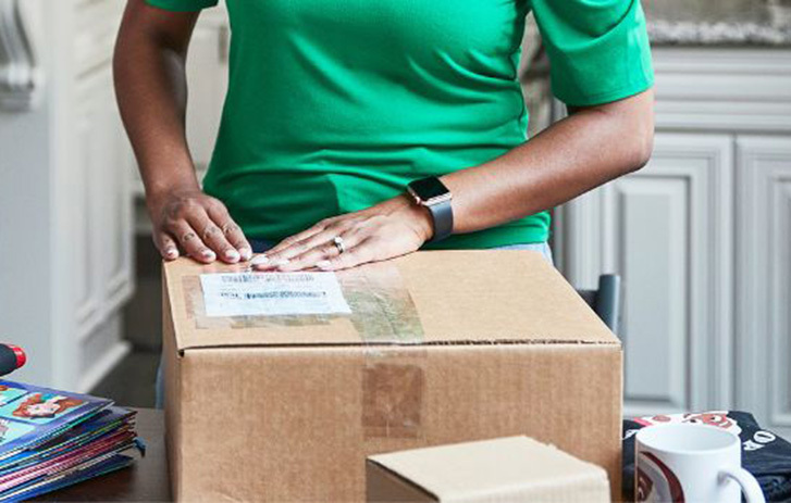 Inhaber*in eines Kleinunternehmens verpackt Bestellungen in einem Homeoffice-Bereich mit Versandmaterial.