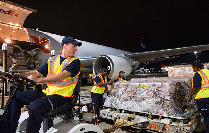 Trabalhadora da FedEx a conduzir um porta-paletes ao lado de um avião da FedEx