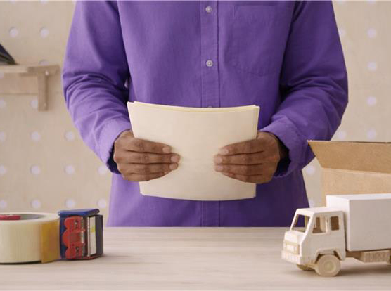 Person holding some papers with a toy truck and packing tape on a table