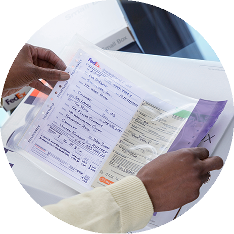 A person holds shipping documents on top of of a FedEx box