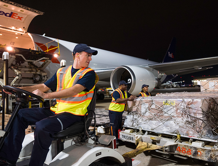 Un employé de FedEx conduisant un chariot de palettes à côté d’un avion FedEx