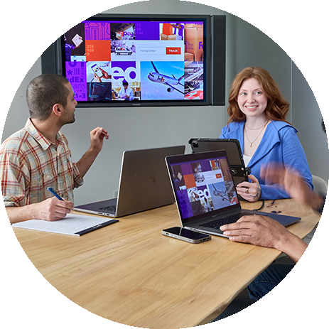 3 coworkers sitting at a conference table in a meeting room with the FedEx Tracking page on a monitor