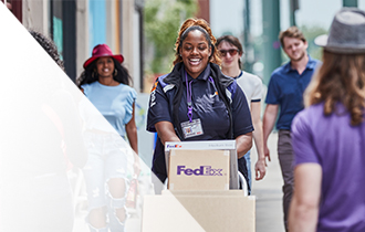 Smiling FedEx courier walks with boxes on the sidewalk in the U.S.