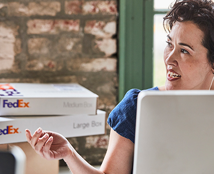 Persoon aan bureau reikt langs een middelgrote of grote FedEx Box op een ander bureau