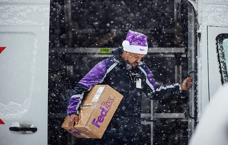 FedEx worker exiting van carrying a package in the snow