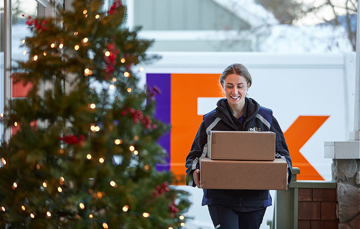FedEx Mitarbeiterin, die neben Weihnachtsdeko Pakete trägt