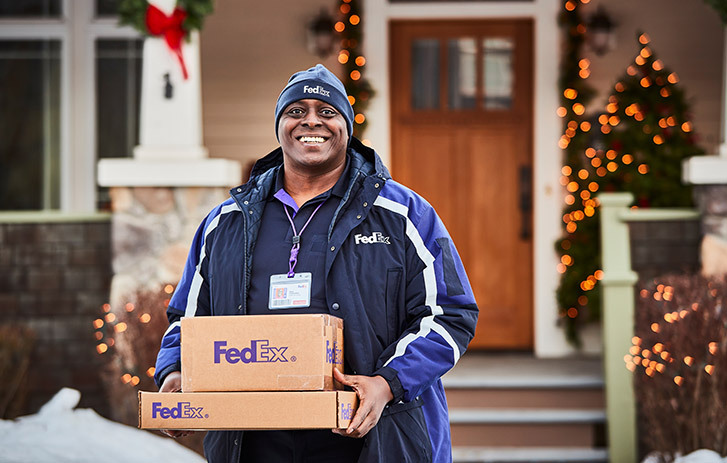 Funcionário sorridente da FedEx a segurar volumes em frente a uma casa