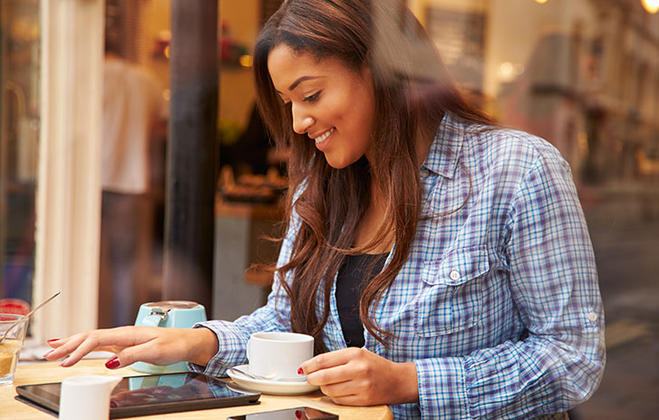Femme regardant une tablette en buvant un café