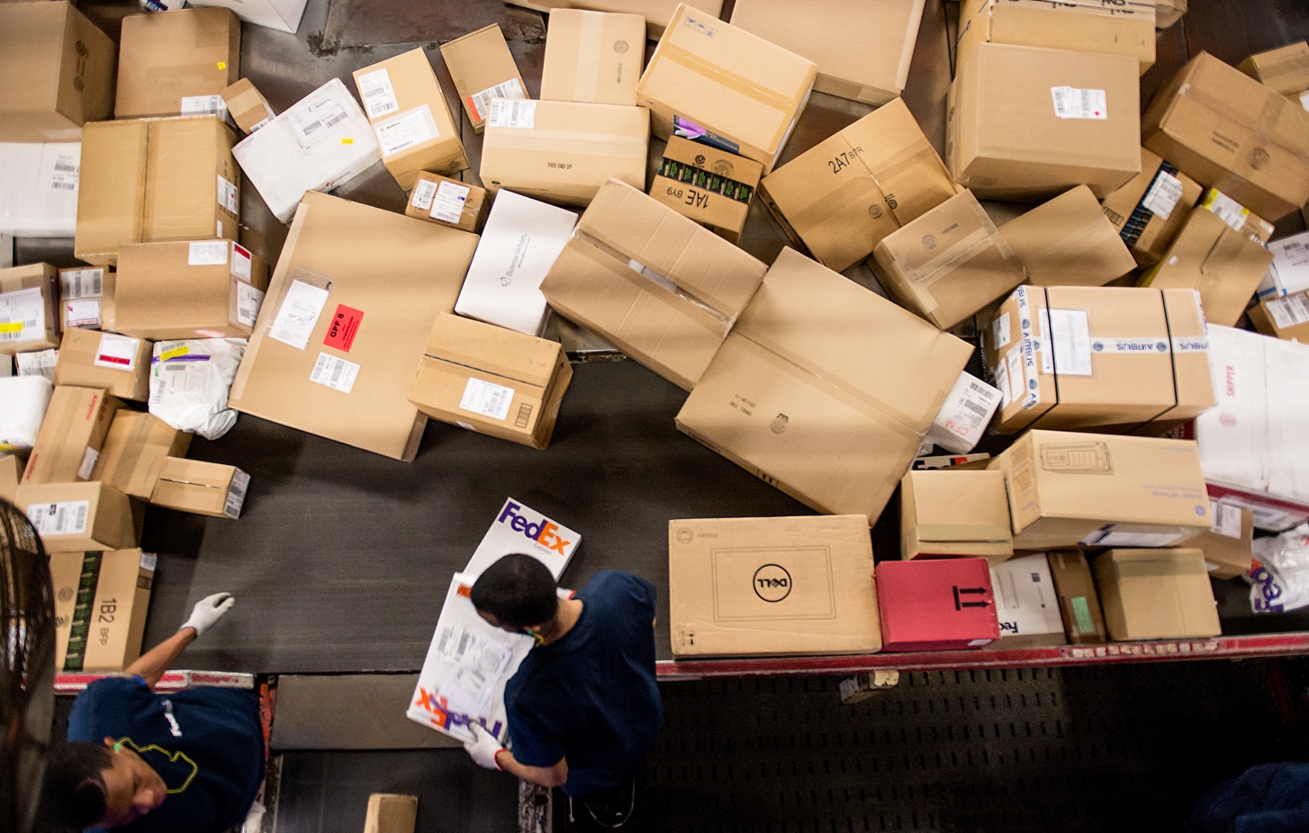 2 FedEx employees processing boxes on a conveyor belt.